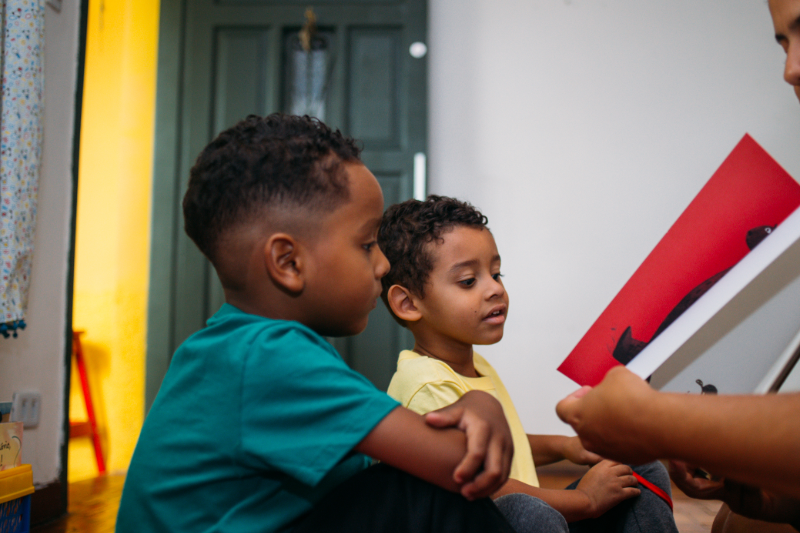 Dois meninos negros olham para um livro ilustrado. A imagem ilustra a matéria "Columbia University abre inscrições em seminário sobre primeira infância para editores brasileiros".