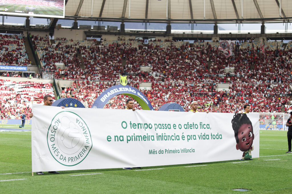 Faixa com Nelson, o Nenê, e os dizeres em destaque "O tempo passa e o afeto fica, e na primeira infância é pra vida toda - Mês da primeira infância", em partida no Maracanã de Flamengo e Grêmio.