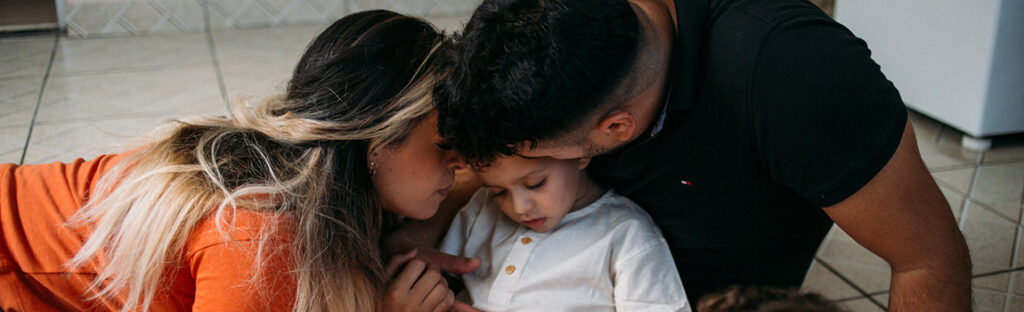 Uma mãe e um pai abraçam um menino de cerca de cinco anos