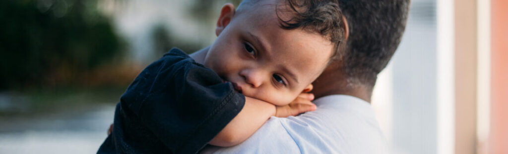 um menino está no colo de seu cuidador. ilustra matéria sobre o cadúnico.