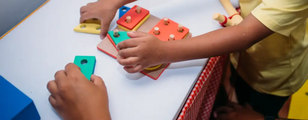 Fotografia que enfoca as mãos de uma criança pequena montando um jogo de encaixar de madeira. A imagem ilustra o posicionamento da Fundação Maria Cecilia Souto Vidigal sobre o homeschooling.